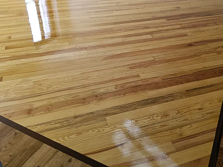 Pavimento in legno a listoni appena levigato e lucidato, con la luce della finestra che si specchia sulla superficie