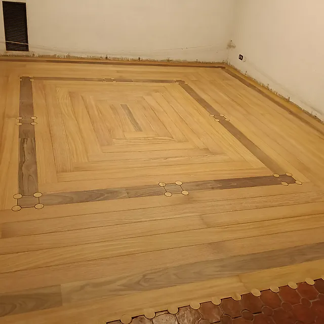 Pavimento in legno con doppia bordura perimetrale e inserti a intarsio, posato al posto del vecchio cotto ancora visibile sul bordo